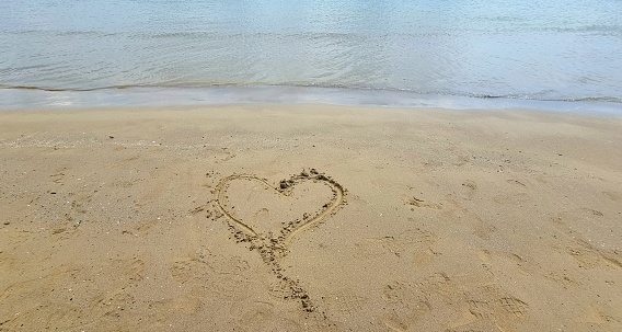 Stock photo of Heart drawn on sunny beach in sand with stick, by sea waves, concept social media photo of hand drawn drawing in soft golden sand on Bournemouth beach, Dorset, England seaside coastline view