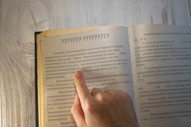 A person leads a finger on the lines in the book, but instead of letters only question marks on the page in the textbook stock photo