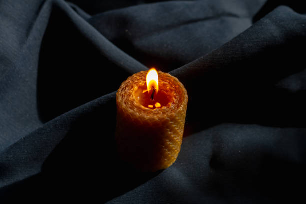 istock A large wax candle with a honeycomb texture on a dark blue fabric burns with a flame 1396315064
