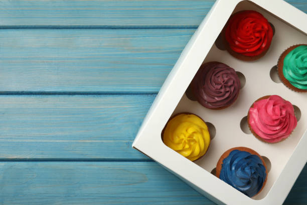 istock Box with different cupcakes on light blue wooden table, top view. Space for text 1396315242