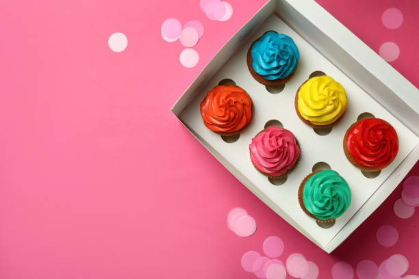 istock Box with different cupcakes and confetti on pink background, flat lay. Space for text 1396315353