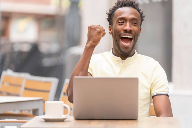 istock Excited man with black skin checking laptop computer celebrating in a bar terrace 1396315439