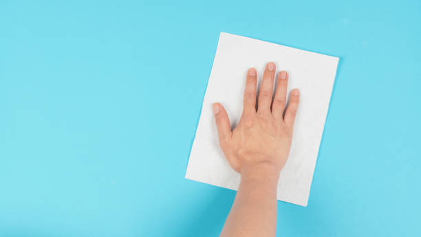 istock Hand is wiping and hold white paper tissue on blue background. Empty space for text . Top down view. 1396317945