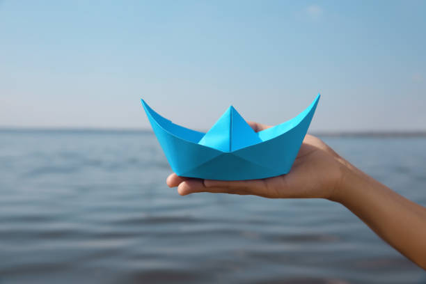 istock Child holding blue paper boat near river, closeup 1396319949