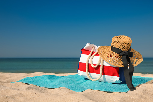 Turquoise beach towel with hat and bag on sand near sea, space for text