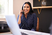 Young indian businesswoman talking on a telephone in an office alone. One female only making a call while working as a receptionist at a front desk. Administrator and secretary consulting and transferring calls from a help desk in a call centre
