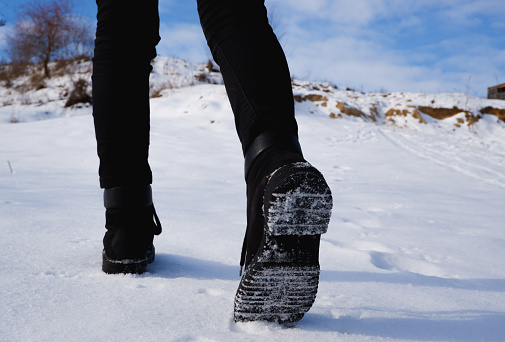 A teenage girl in black jeans and boots walks uphill through the dense snow. Close-up shot of the legs from behind.