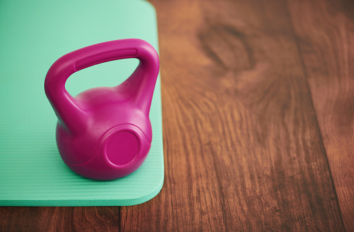 Yoga mat on a hardwood floor with a pink kettlebell for working out. Health and wellness concept with copy space
