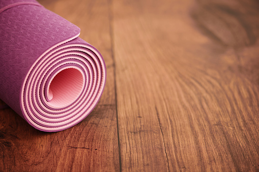Yoga class background with rolled up pink yoga mat on a wooden floor. Heathy lifestyle concept with copy space