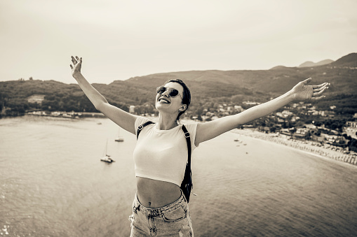 Young attractive happy woman with her hands up enjoying on vacation with amazing sea view