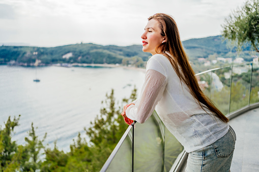 Young woman standing on the balcony of a restaurant and enjoying the sea view
