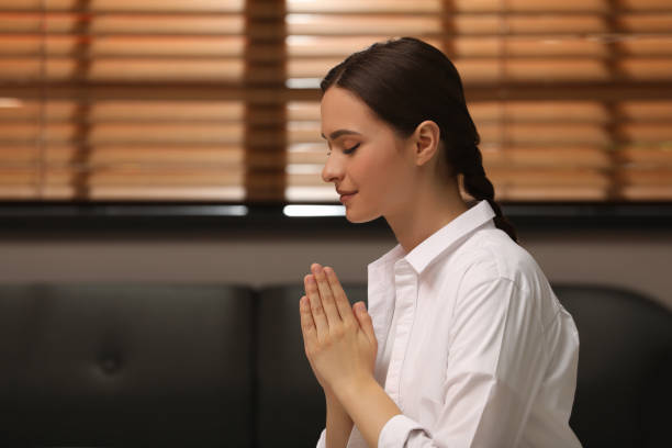 istock Religious young woman with clasped hands praying indoors 1396327000