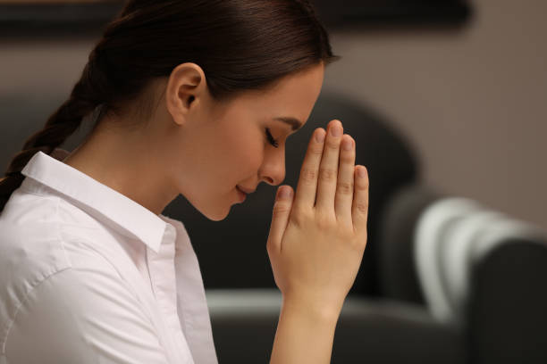 istock Religious young woman with clasped hands praying indoors 1396327305