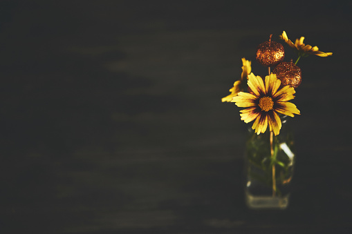 Low key image of a vase of yellow flowers with a rustic wood background and copy space