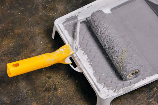 istock Paint roller with yellow handle in tray for roller with gray paint on concrete floor. 1396328769