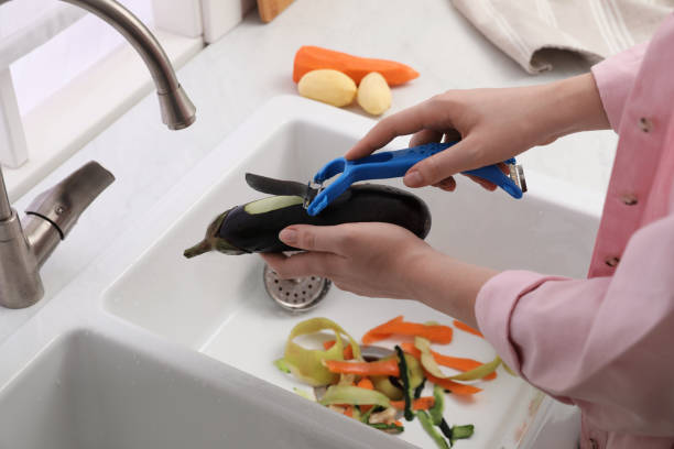 woman peeling cucumber over kitchen sink with garbage disposal at home, closeup - sink domestic kitchen kitchen sink faucet imagens e fotografias de stock