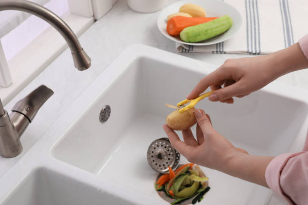 woman peeling potato over kitchen sink with garbage disposal at home, closeup - sink domestic kitchen kitchen sink faucet imagens e fotografias de stock