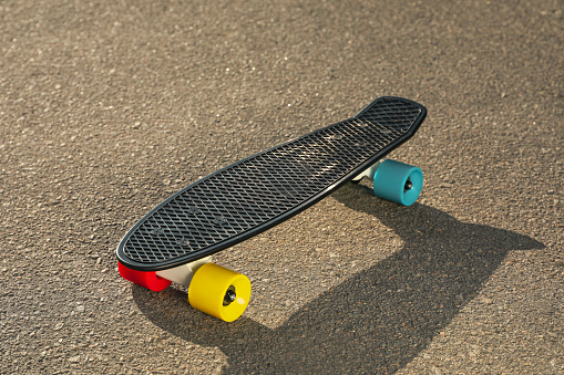 Black skateboard with colorful wheels on asphalt outdoors