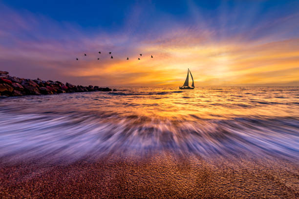 A Sailboat Silhouette Sailing Against A Colorful Sunset Sky And A Flock Of Birds Flying Overhead