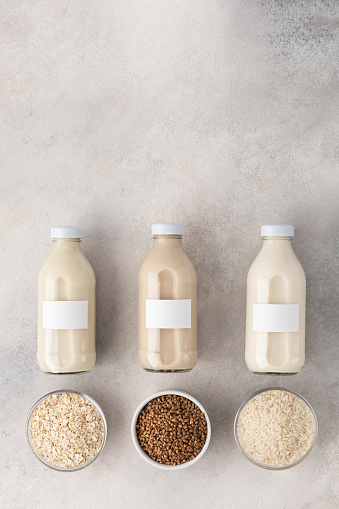 Bottles with vegetable milk: oatmeal, buckwheat and rice with ingredients on a light background