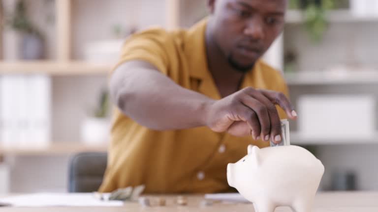 A shot of coins and a piggy bank on a table with an young businessman working in the background