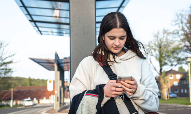 istock A young woman uses a smartphone while standing at a bus stop. 1396334457
