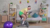istock Funny energetic man athlete from the 80s with a mustache engaged at home on a exercise bikee slow mo 1396334615