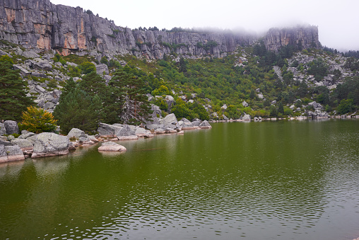 A lake surrounded by rock formations and a lush pine forest under a gray sky.