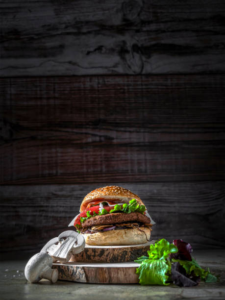 Vegan burger with mushrooms Hamburger with chickpea patty, tomato, mushrooms and vegetables on rye bread. Around, mushrooms and salad. Copy space. Vertical shot spanish hamburger stock pictures, royalty-free photos & images