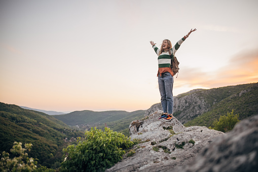 One woman, young female hiker standing on a rock high on mountain in sunset.