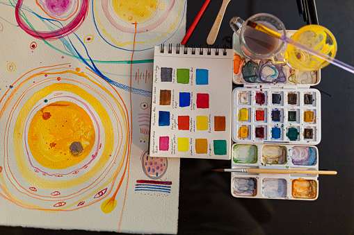 Creative space of an artist, watercolor palette, water, paint brushes and colored paper.