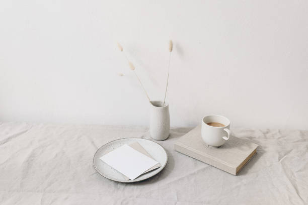 istock Neutral breakfast still life scene. Blank greeting card, ceramic plate. Vase with dry lagurus bunny tail grass on book. Cup of coffee on book. Linen table cloth, white wall. Scandinavian interior. 1396346769