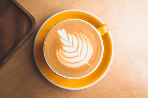 Taza de café capuchino con rosetta latte art se encuentra en un escritorio de madera photo