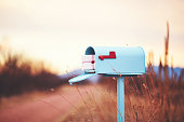Teal mailbox filled with a stack of love letters on a rural path at dusk
