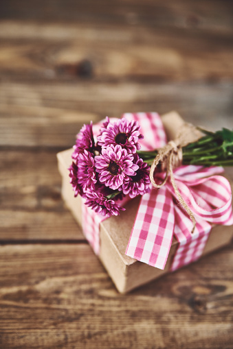 Small gift box on a wooden table with a bunch of pink flowers and copy space