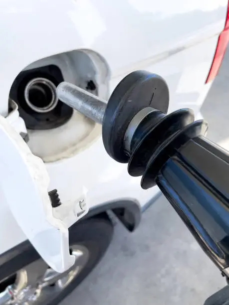 close-up of black gas pump nozzle being inserted into gas tank on white car at the gas station.