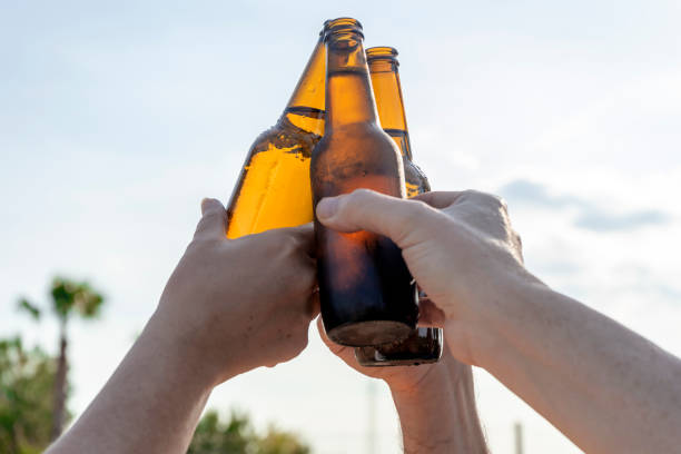 eine gruppe von freunden feiert und klirrt bierflaschen im freien bei sonnenuntergang. übermässiger alkoholkonsum von minderjährigen. fokus ausgewählt. - beer bottle beer bottle alcohol stock-fotos und bilder
