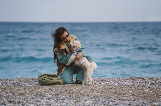 Young woman sitting on the beach playing with her terrier puppy