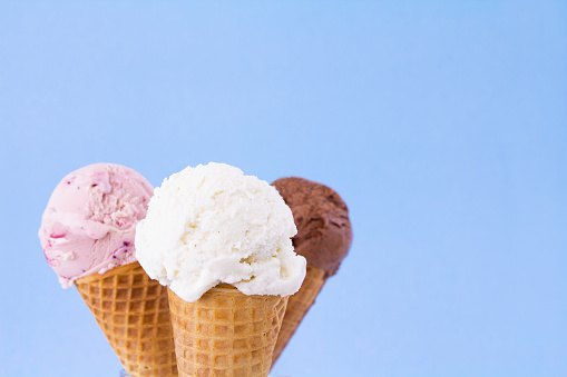 Strawberry, chocolate and vanilla ice cream in  sugar cones, on a pastel blue background.