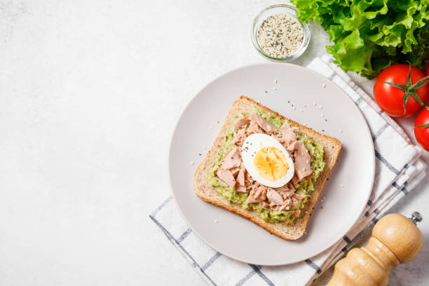Avocado rye bread toast with tuna and boiled egg on bright background. Healthy appetizer, breakfast, lunch or snack. Copy space, top view stock photo