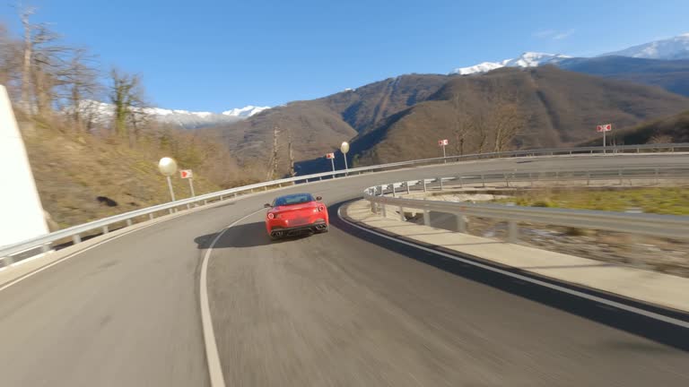 FPV drone freestyle shooting red sport car driving on serpentine asphalt mountain road