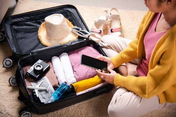 istock Woman using smartphone blank screen and packing suitcase bag for travel trip weekend vacation at home 1396364346