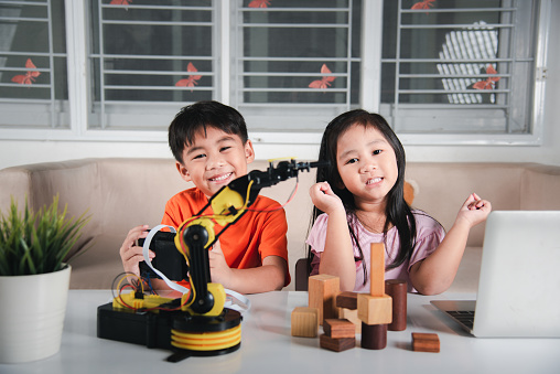 Two children programming and testing robot arm their science, Kid little girl program code to robot with laptop computer and the boy test with remote control to pick up wood block, education lesson