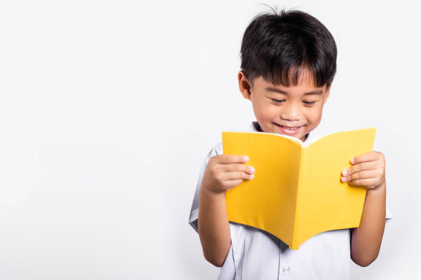 Asian toddler smile happy wearing student thai uniform red pants standing holding and reading a book stock photo