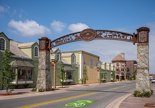 Temecula, CA, USA - April 11, 2022: Old Town neighborhood. SE side rusted metal historic street portal and sculpture with line of buildings under blue cloudscape. Street scenery.