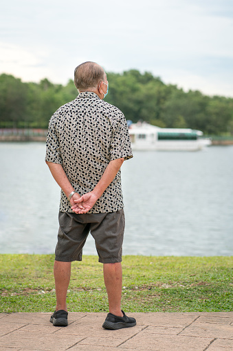 Rear view of senior asian man looking out at a lake horizon. Travel or vacation concept.