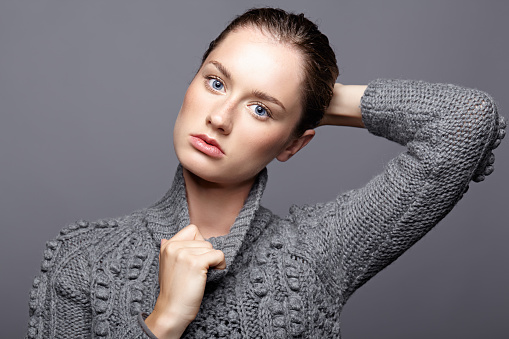 Beauty portrait of young woman in gray wool sweater. Brunette girl with bright blue eyes and day female makeup.