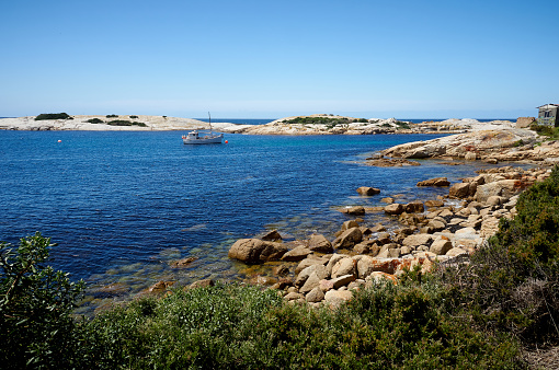 Summer day with no people on a cove in Bicheno near the jetty.  The orange lichen covered rocks contrast with the deep blue of the ocean and no clouds in the sky.