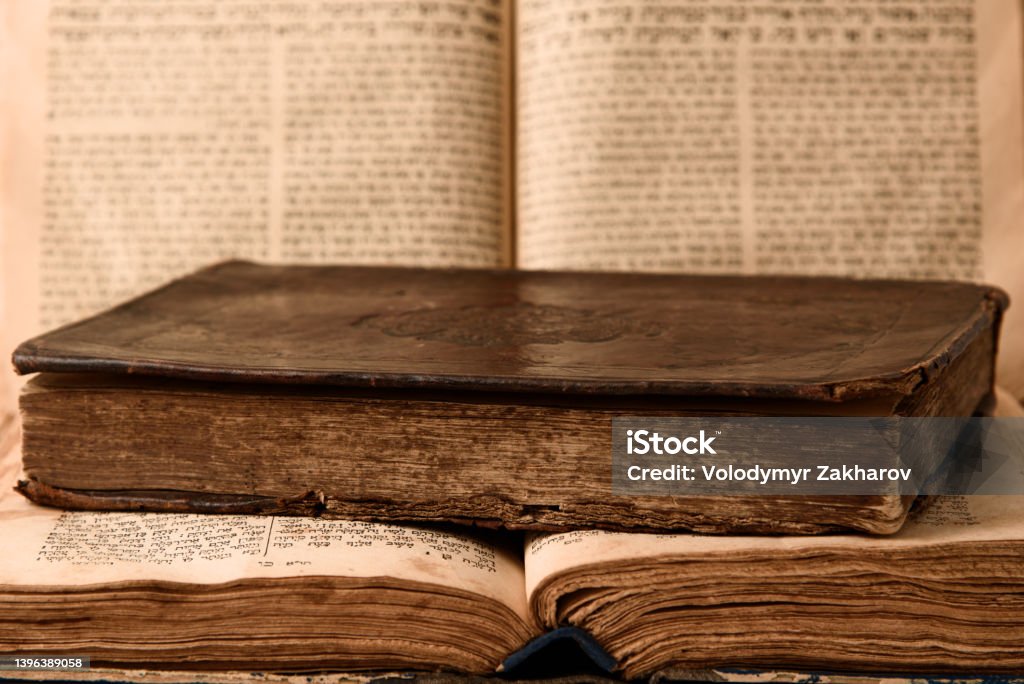 Old worn shabby jewish books in leather binding and open blurred Torah in the background. Closeup. Selective focus. Old worn shabby jewish books in leather binding and open blurred Torah in the background. Closeup. Selective focus Book Stock Photo