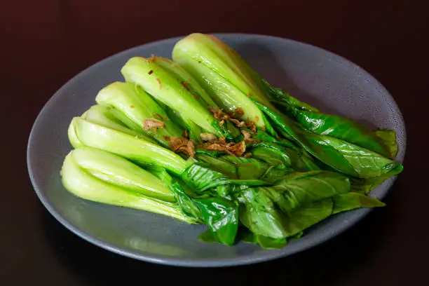 Stir-fried bok choy of traditional Cantonese yum-cha Asian gourmet cuisine meal food dish on the serving plate and brown red table